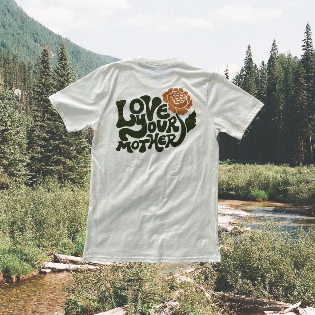Image features the back of the sustainably made 100% organic cotton Love Your Mother tee by Be Kind Vibes overlaid on a photo of the British Columbia wilderness.