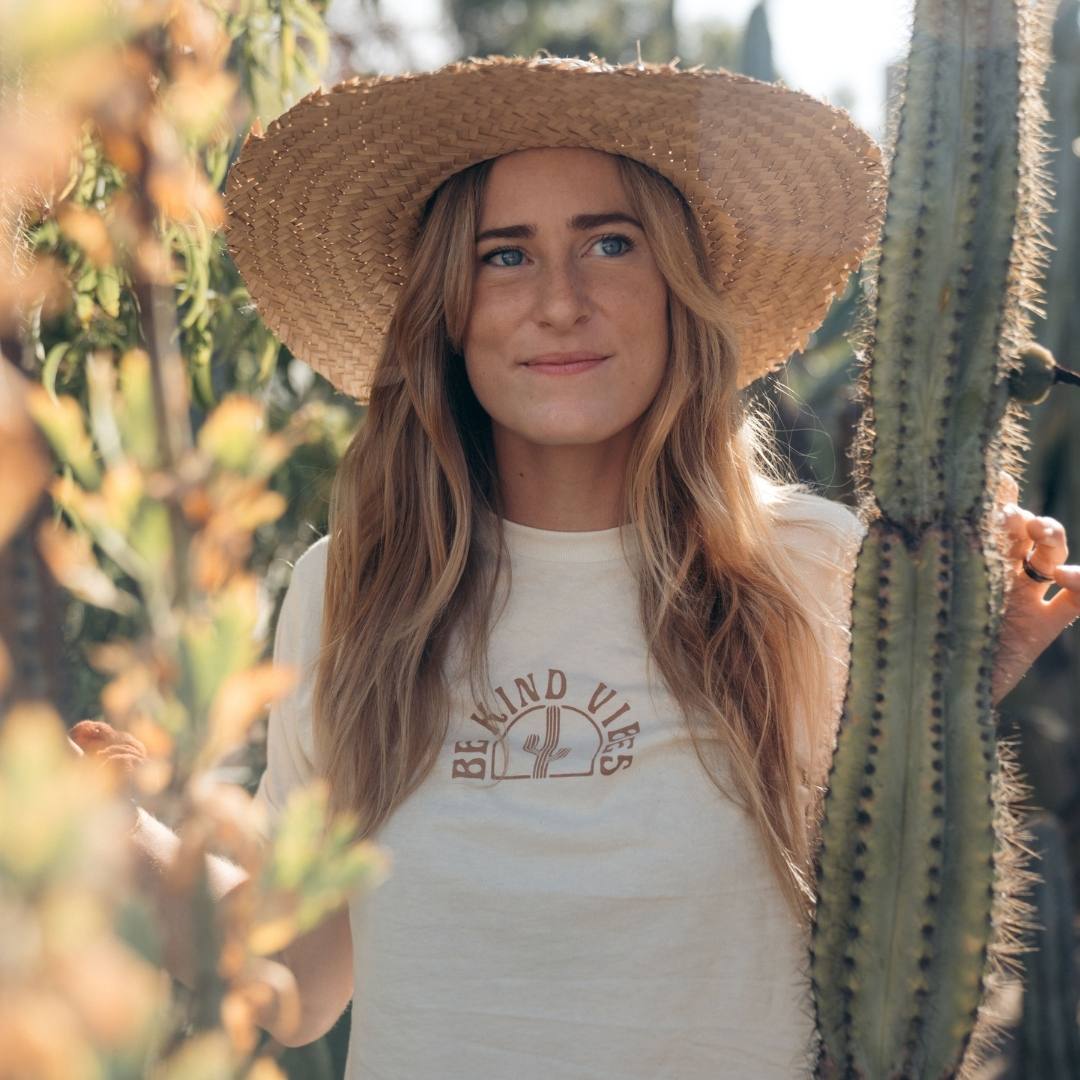 A front facing hero image featuring a female model wearing the Be Kind Vibes Desert crop top in natural