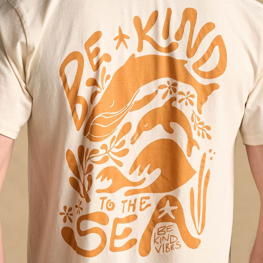 Image features the back of a male model wearing the 100% organic cotton eco-friendly Be Kind Vibes Be Kind to the Sea t-shirt with a design that features a whale, dolphin, ocean plants and the text Be Kind to the Sea Over the top and bottom.