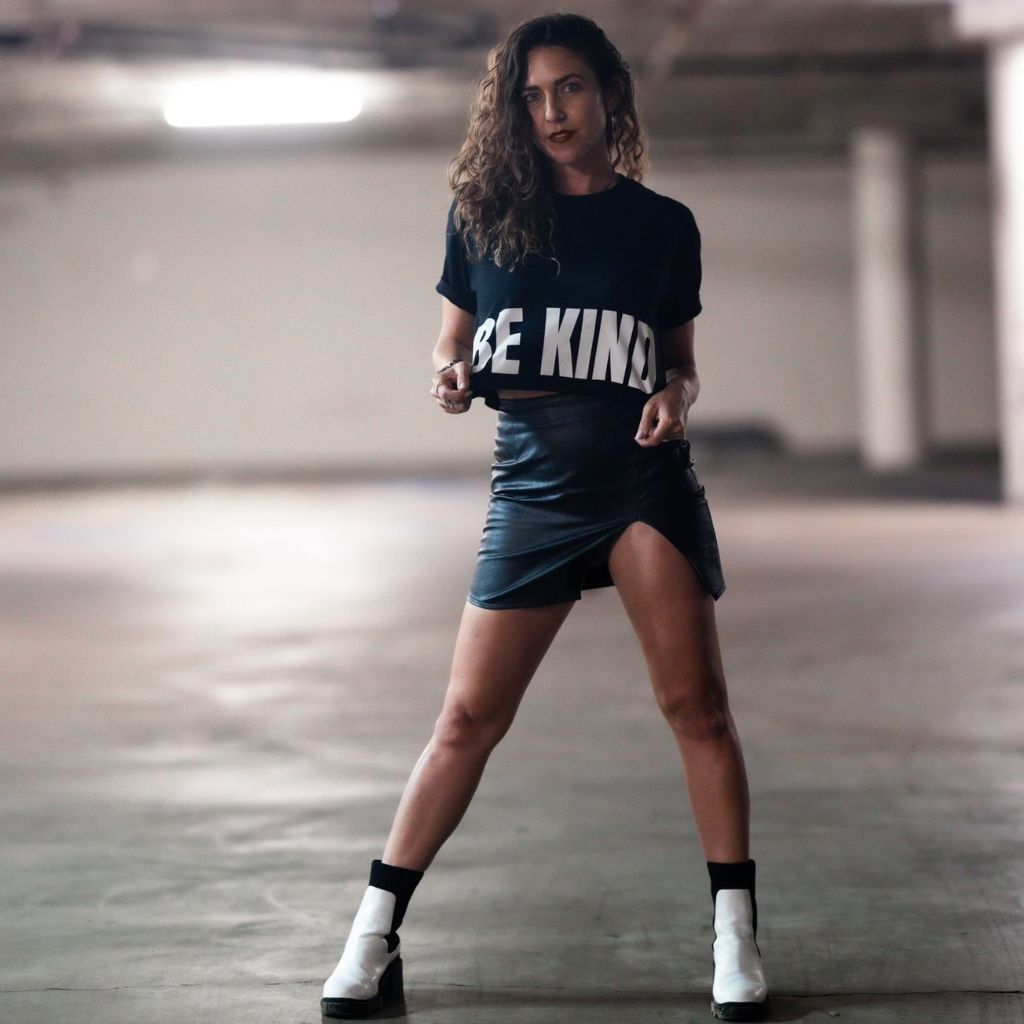 Image features a female model wearing a black leather mini skirt, white boots, and the Be Kind Vibes black BE KIND crop top