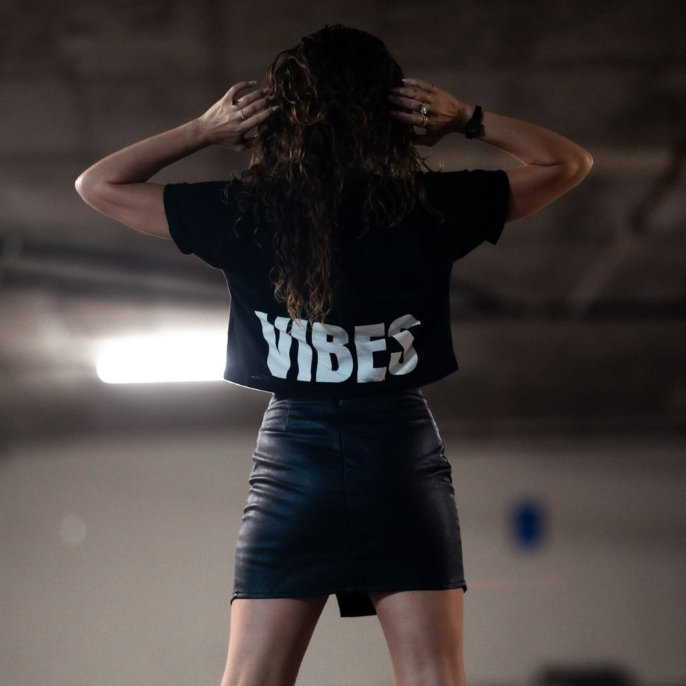 
                  
                    Image features the back of a female model wearing a black leather mini skirt and the black Be Kind Vibes Be Kind crop top. The model is standing in a parking garage.
                  
                