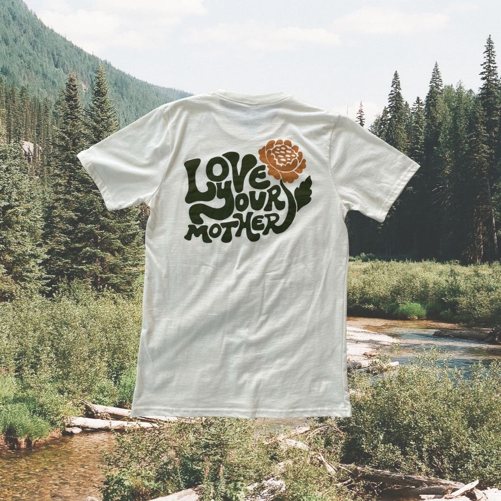 
                  
                    Image features the back of the sustainably made 100% organic cotton Love Your Mother tee by Be Kind Vibes overlaid on a photo of the British Columbia wilderness.
                  
                