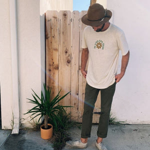 Image featuring a male model in a brown hat, green pants, and white shoes wearing the Be Kind Vibes sustainably made Be Kind & Shine tee in natural.