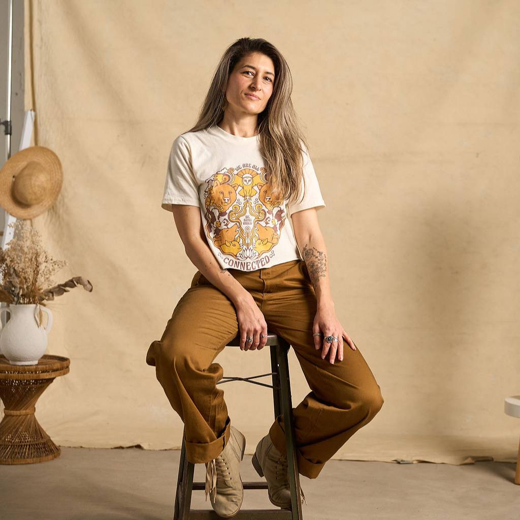 
                  
                    Hero image features a female model wearing the Be Kind Vibes We Are All Connected crop top with an animal design on the front featuring bears, cows, chickens, wolves, pigs, and an owl. The model is sitting on a stool wearing copper colored pants.
                  
                