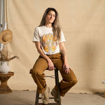 Hero image features a female model wearing the Be Kind Vibes We Are All Connected crop top with an animal design on the front featuring bears, cows, chickens, wolves, pigs, and an owl. The model is sitting on a stool wearing copper colored pants.