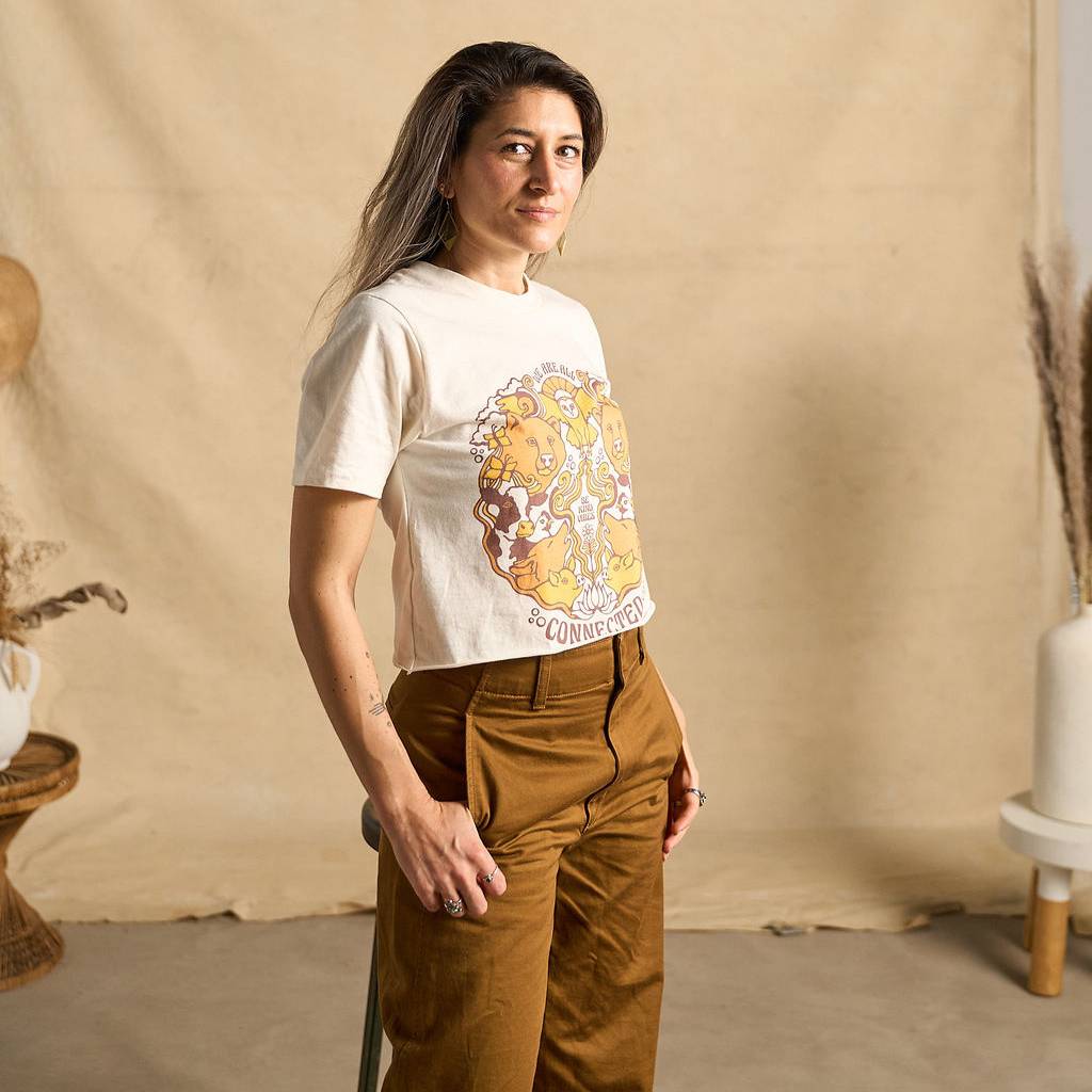 Hero image features a female model wearing the Be Kind Vibes We Are All Connected crop top with an animal design on the front featuring bears, cows, chickens, wolves, pigs, and an owl. The model is also wearing copper colored pants.