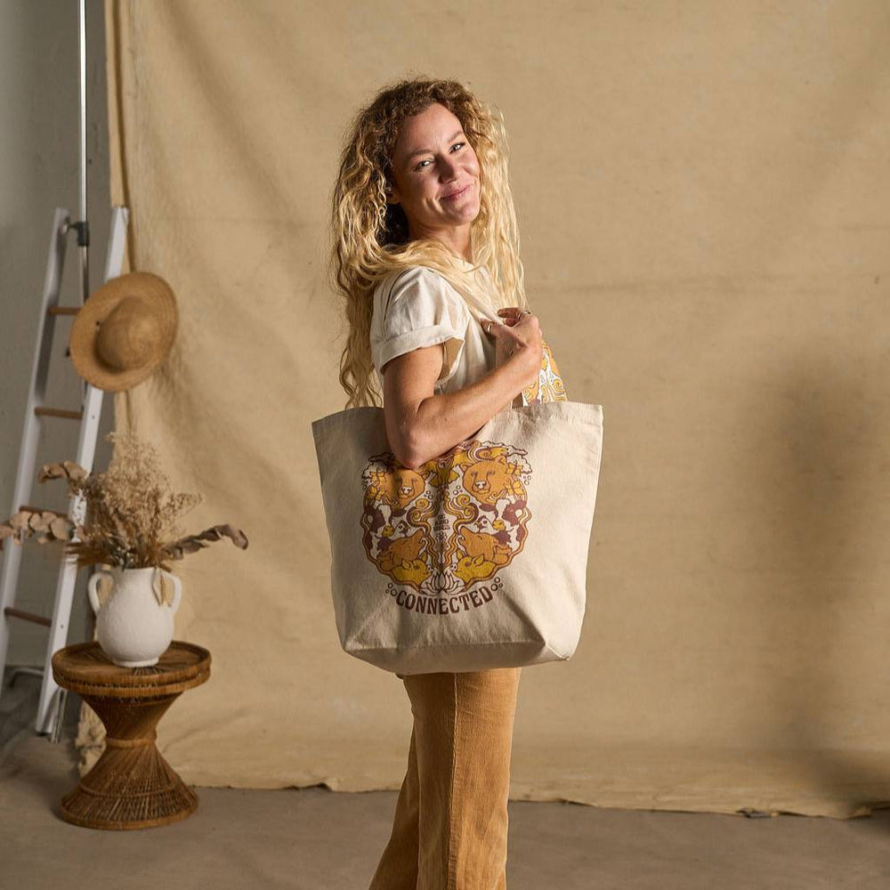 
                  
                    Image features a side angle photo of a female model standing in front of a beige fabric backdrop. She's wearing a natural colored t-shirt, brown khaki pants, and is holding the Be Kind Vibes We Are All Connected tote bag over her shoulder.
                  
                