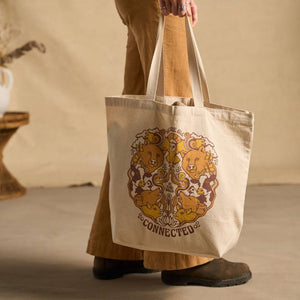 Image features a side angle shot of a female model wearing light brown khakis holding the Be Kind Vibes We Are All Connected tote bag in natural off to the side.