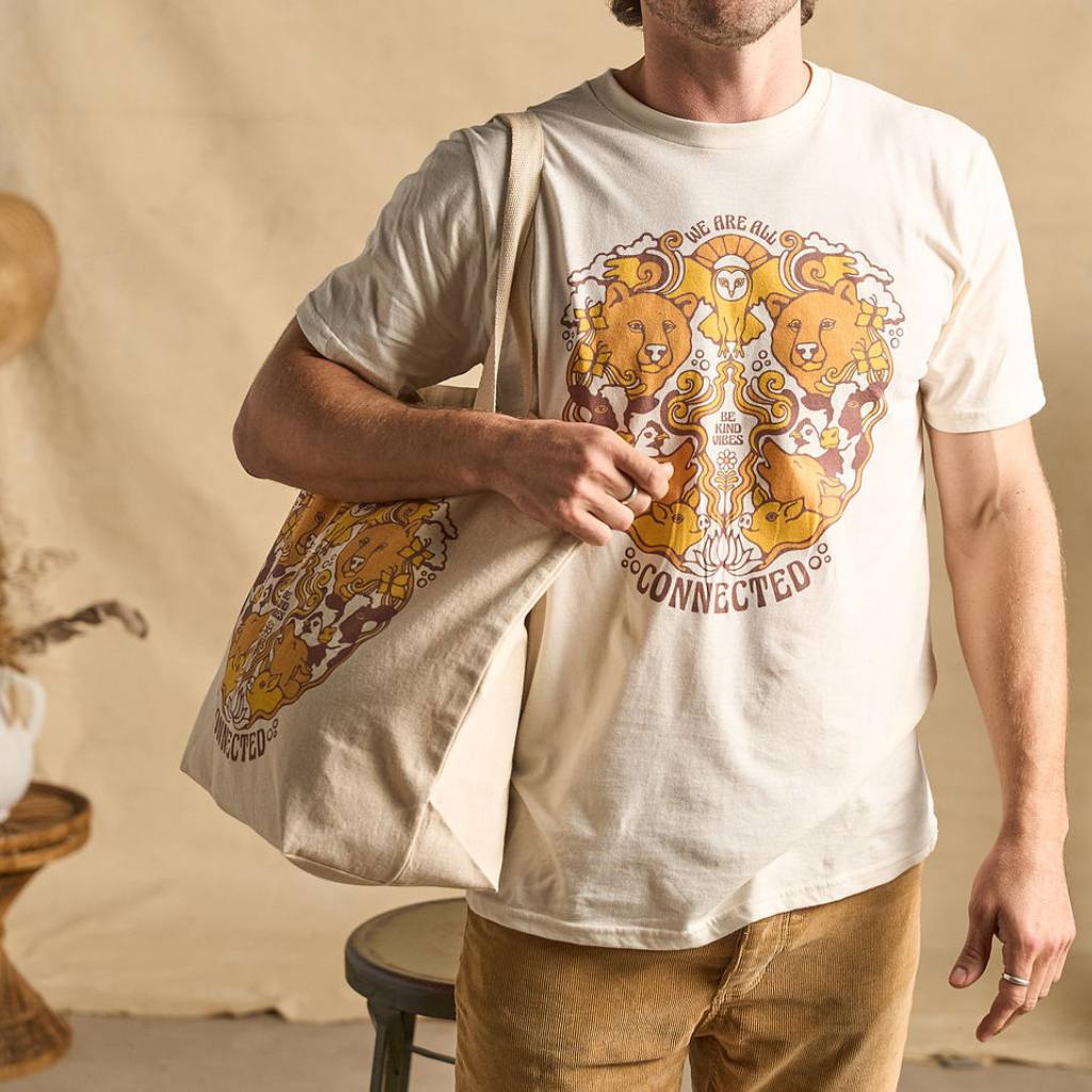 
                  
                    Image features a male model holding the Be Kind Vibes We Are All Connected tote bag over his right shoulder. He's wearing the We Are All Connected t-shirt, light brown khaki pants, and is standing in front of a beige fabric backdrop.
                  
                