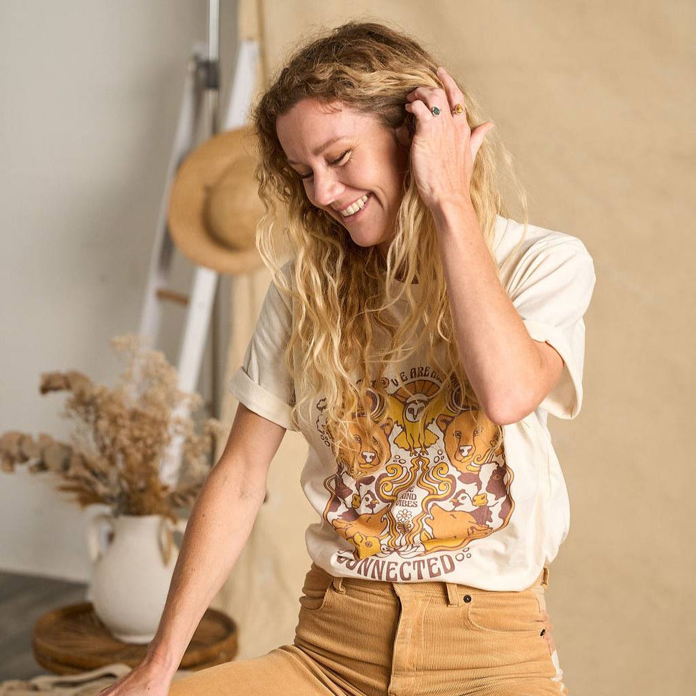 
                  
                    Image features a female model wearing the Be Kind Vibes We Are All Connected t-shirt with an animal design on the front featuring bears, cows, chickens, wolves, pigs, and an owl. The model is wearing light brown khakis and is standing in front of a beige fabric backdrop.
                  
                