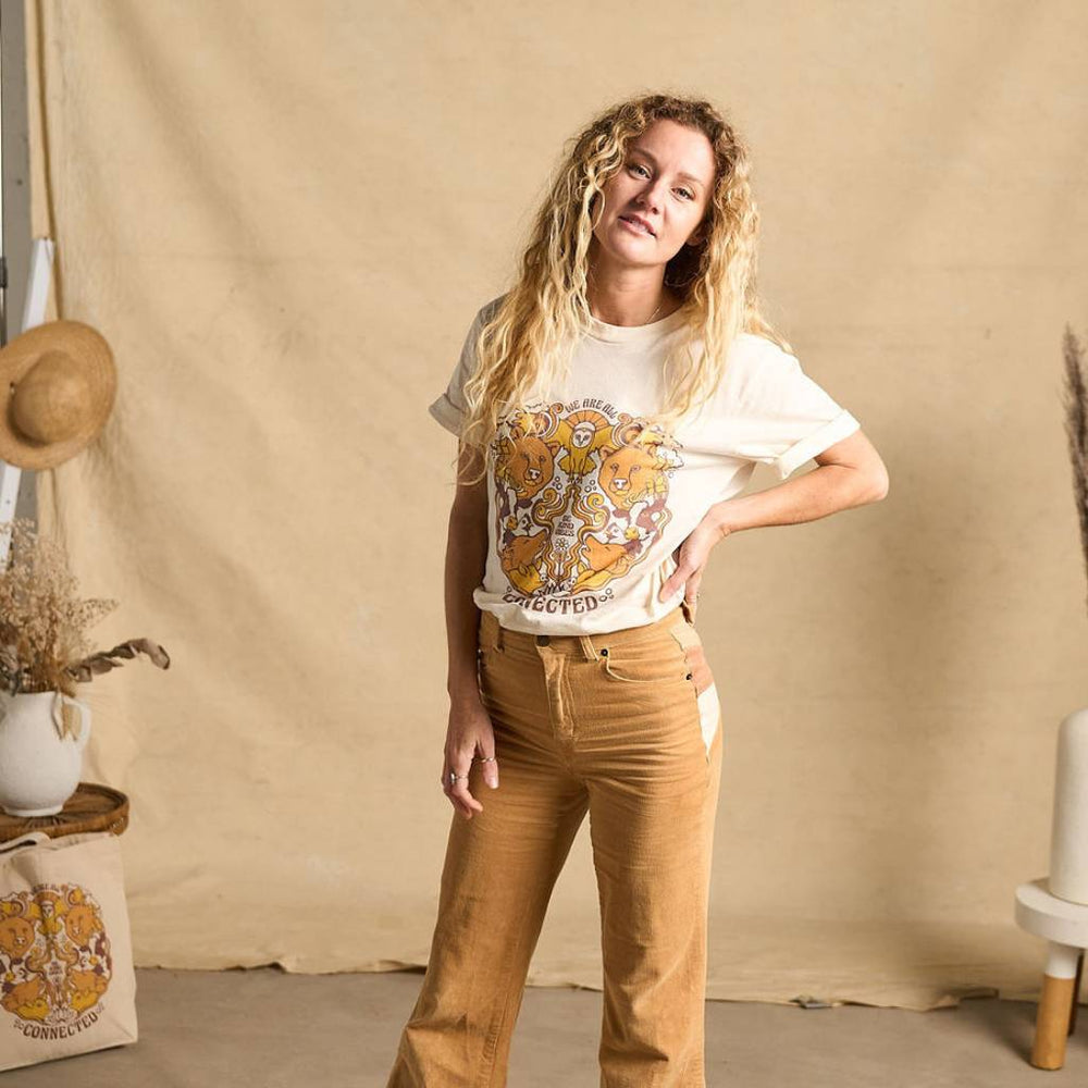 
                  
                    Image features a female model wearing the Be Kind Vibes We Are All Connected t-shirt with an animal design on the front featuring bears, cows, chickens, wolves, pigs, and an owl. The model is wearing light brown khakis and is standing in front of a beige fabric backdrop.
                  
                