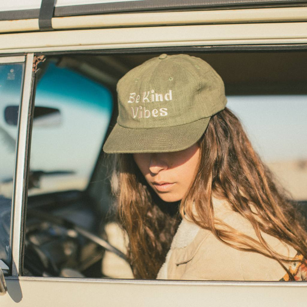 
                  
                    Image features a female model leaning out of the driver side seat of a VW bus wearing the cactus colored Be Kind Vibes Be Kind Hemp Hat and a khaki jacket.
                  
                
