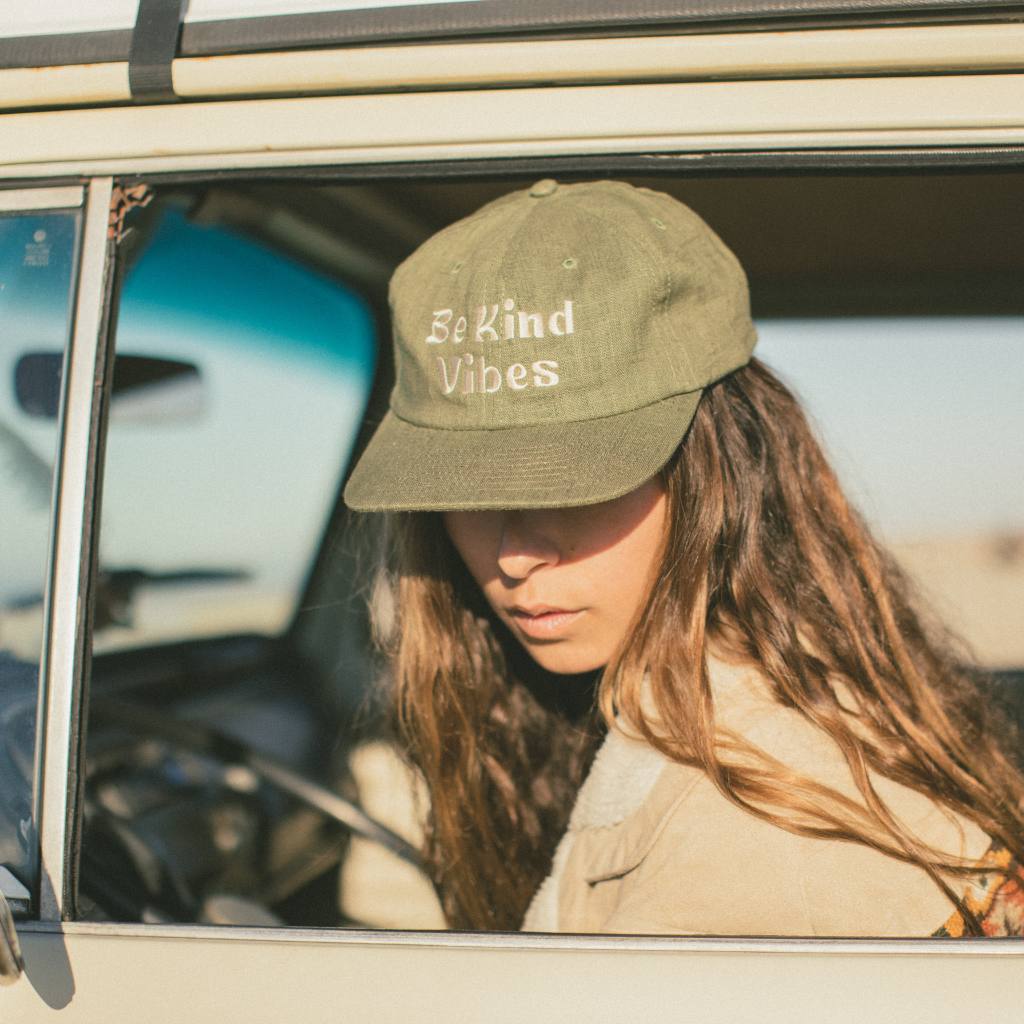 
                  
                    Image features a female model leaning out of the driver side seat of a VW bus wearing the cactus colored Be Kind Vibes Be Kind Hemp Hat and a khaki jacket.
                  
                