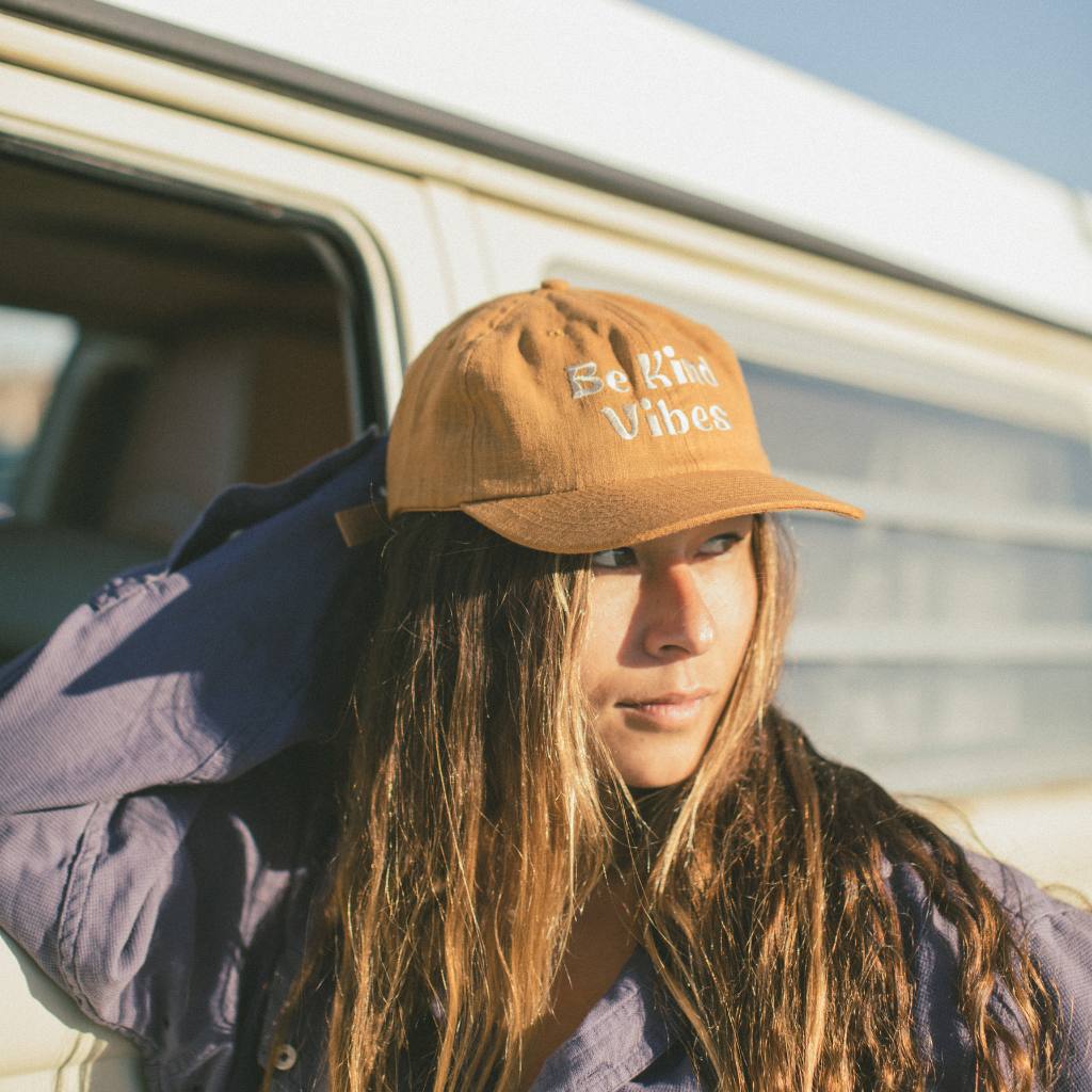 
                  
                    Image features a female model wearing a purple long sleeve and the Be Kind Vibes Be Kind Hemp Hat. Her right hand is holding the back of her head, and she's standing against the driver side of a VW bus.
                  
                