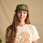 Image features a female model looking directly at the camera wearing the cactus colored Be Kind Vibes Be Kind Hemp hat and the natural colored Be Kind Vibes Be Kind to the Sea organic cotton t-shirt.