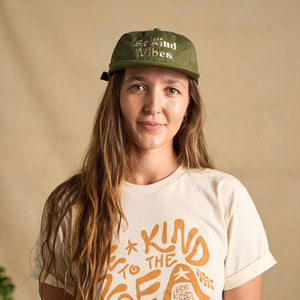Image features a female model looking directly at the camera wearing the cactus colored Be Kind Vibes Be Kind Hemp hat and the natural colored Be Kind Vibes Be Kind to the Sea organic cotton t-shirt.