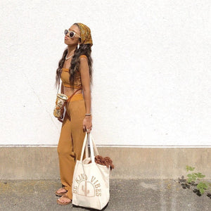 Image features a female model holding the Be Kind Vibes ethically made Desert Tote bag while she leans against a white wall